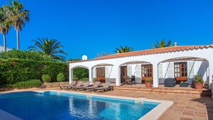 Une piscine avec des chaises longues et un patio couvert aménagé avec du mobilier d’extérieur.