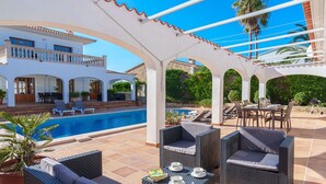 Un espace aménagé au bord de la piscine, avec des sièges extérieurs et une vue sur la piscine et la maison.