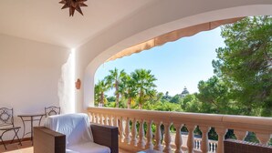 A balcony with wicker furniture, a glass table, and a view of palm trees and greenery. - Nice apartment for 4 guests with pool, WIFI, TV and terrace (Manacor)