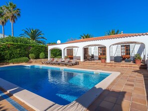 Une piscine avec des chaises longues et un patio couvert aménagé avec du mobilier d’extérieur.