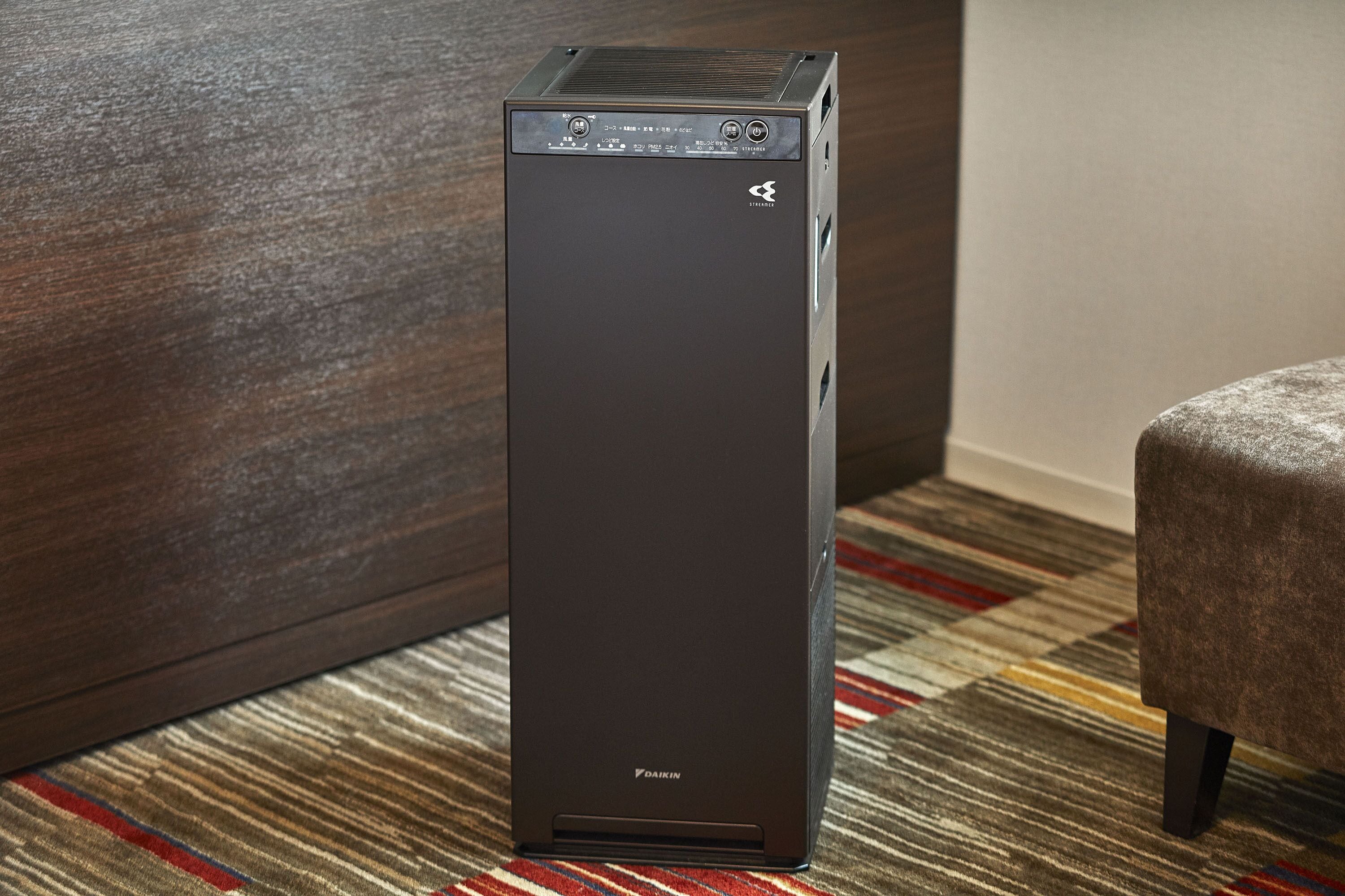 A tall, dark-colored, modern-looking desktop computer in a room with a patterned carpet and a wooden wall.