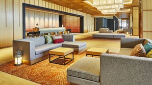 Een ruime lobby met een modern design, met een grote zithoek met banken en fauteuils, een receptiebalie en een decoratieve wand met verticale panelen.