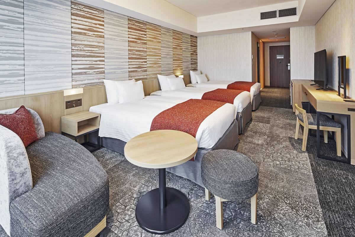 Une chambre d’hôtel avec quatre lits, un bureau, une télévision et une petite table ronde.