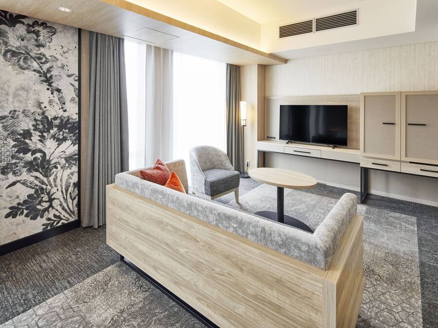 A modern hotel room with a sofa, a TV, a small table, and a cabinet.