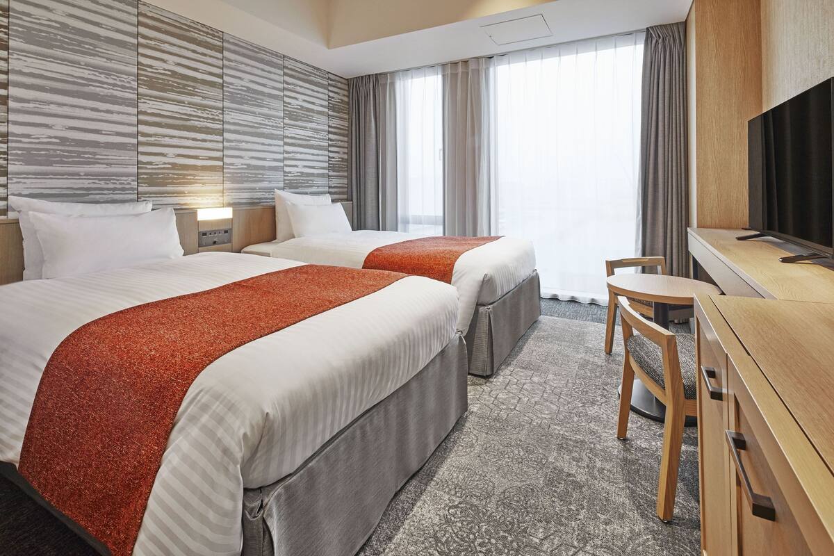 Une chambre d’hôtel avec deux lits, un bureau, une chaise et un téléviseur.