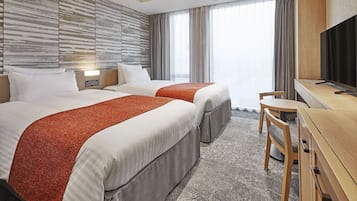 A hotel room with two beds, a desk, a chair, and a television.