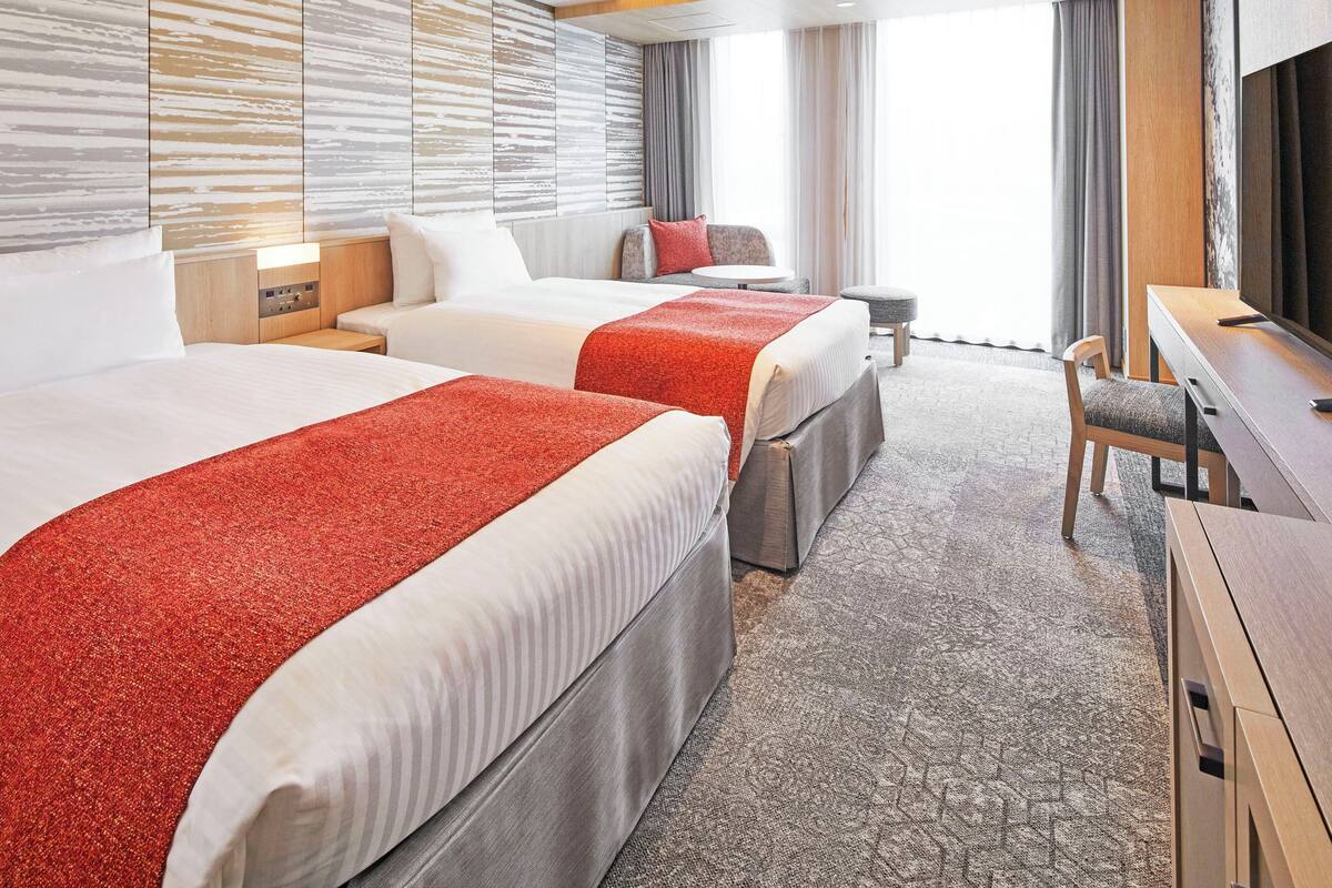 Une chambre d’hôtel avec deux lits, un bureau, une chaise et une grande fenêtre.