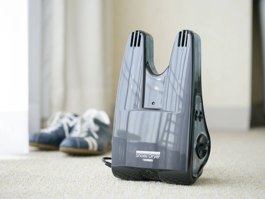 A shoes dryer on a carpeted floor with a pair of shoes in the background.