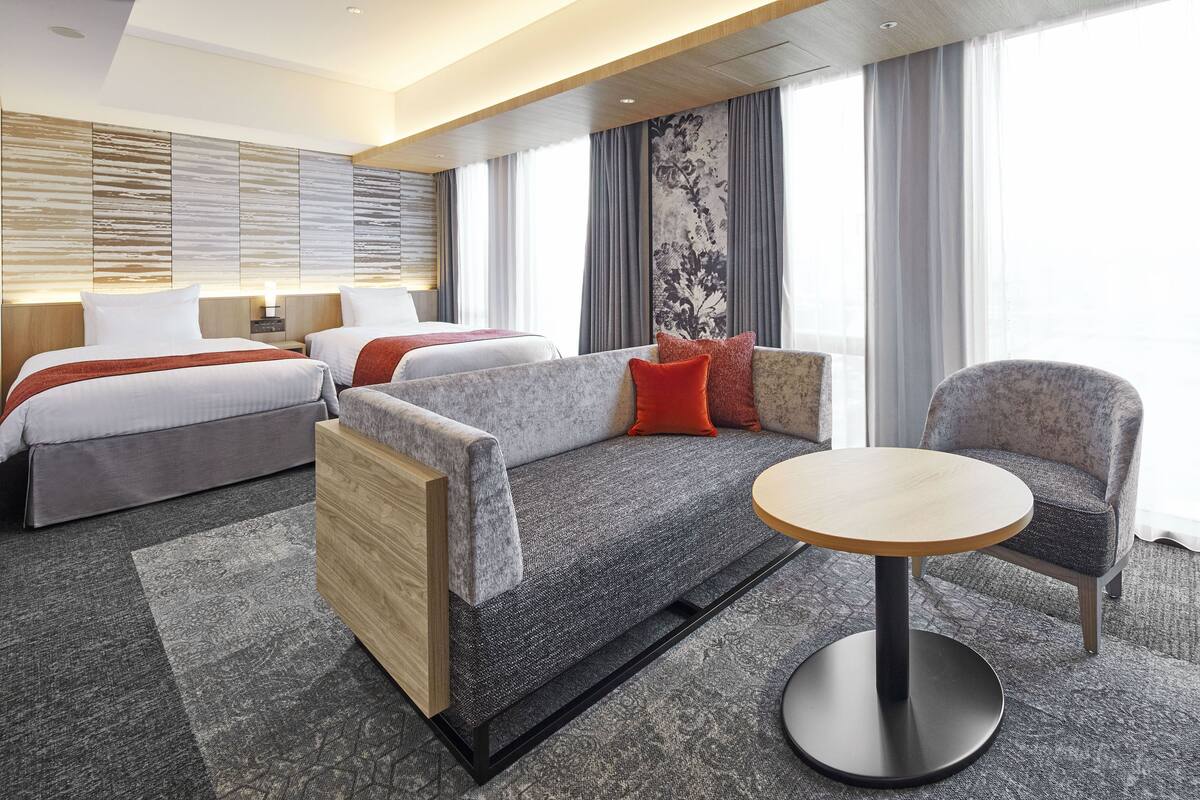 Une chambre d’hôtel moderne équipée d’un canapé-lit, d’une table ronde et d’un fauteuil séparé.