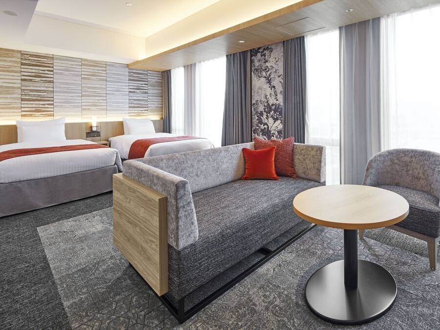 A modern hotel room with a sofa bed, a round table, and a separate armchair.