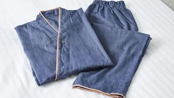 A neatly folded pair of blue pajamas with a button and drawstring on a white bedspread.