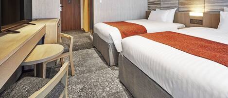 A hotel room with a desk, two beds, a television, and a wall-mounted light.