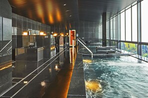 Ein moderner, überdachter Pool mit großen Glaswänden, nassem Boden und Blick auf Grünflächen im Freien.