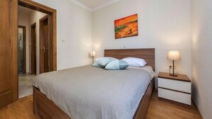 Un dormitorio con cama de madera, mesita de noche, un cuadro en la pared y una puerta que da a otra habitación.