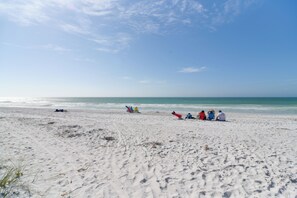 En sandstrand med folk, der sidder og går langs kysten.