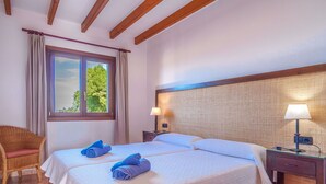 Une chambre d’hôtel avec deux lits, une fenêtre avec des rideaux, un fauteuil en osier et une table de chevet avec une lampe.