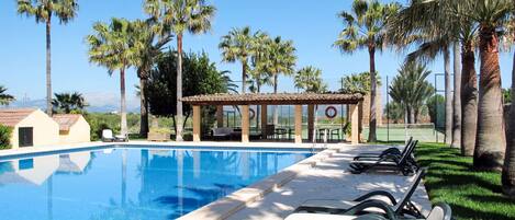 A swimming pool with lounge chairs, palm trees, and a covered seating area.