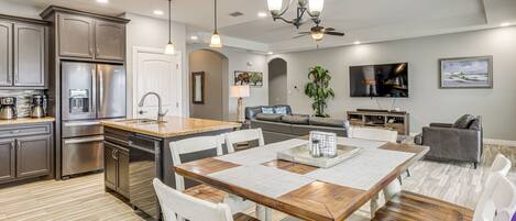A modern kitchen with stainless steel appliances, a wooden dining table, and a living area with a TV and seating.