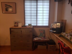 A room with a wooden dresser, a window with blinds, a coffee machine, a map collection, and a red chair.