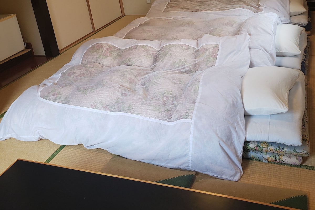 A neatly made bed with a floral-patterned duvet, a wooden floor, and a traditional Japanese sliding door.
