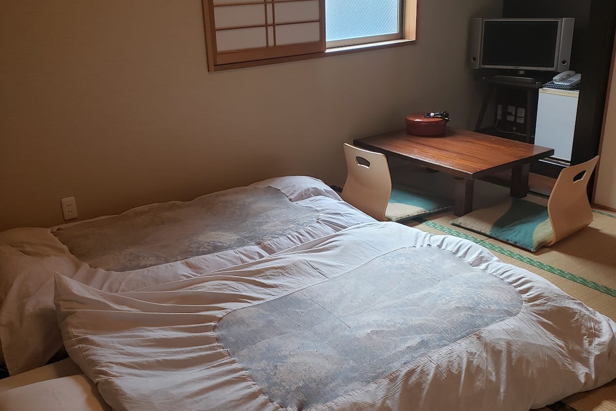 A room with a bed, a desk, a television, and a small refrigerator.