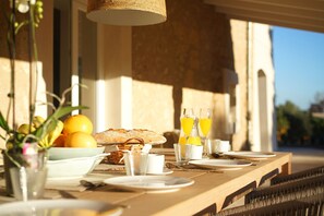 Une table de petit-déjeuner dressée avec des assiettes, des verres et un panier de pain et de fruits.