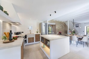 A modern kitchen with a central island, built-in appliances, and a dining area with a view. - Villa Antigua (Pollensa)