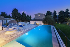 A swimming pool with lounge chairs and a slide, surrounded by trees and a stone building.