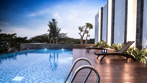 A swimming pool with a tiled edge, lounge chairs, and a wooden deck. - Aston Sidoarjo City Hotel & Convention Center (Sidoarjo)