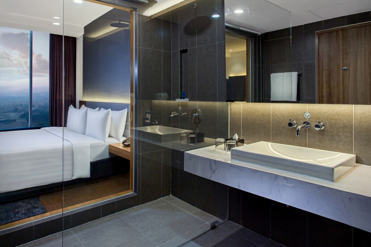 Una habitación de hotel moderna con una cama grande, cabina de ducha con paredes de vidrio y tocador de mármol.