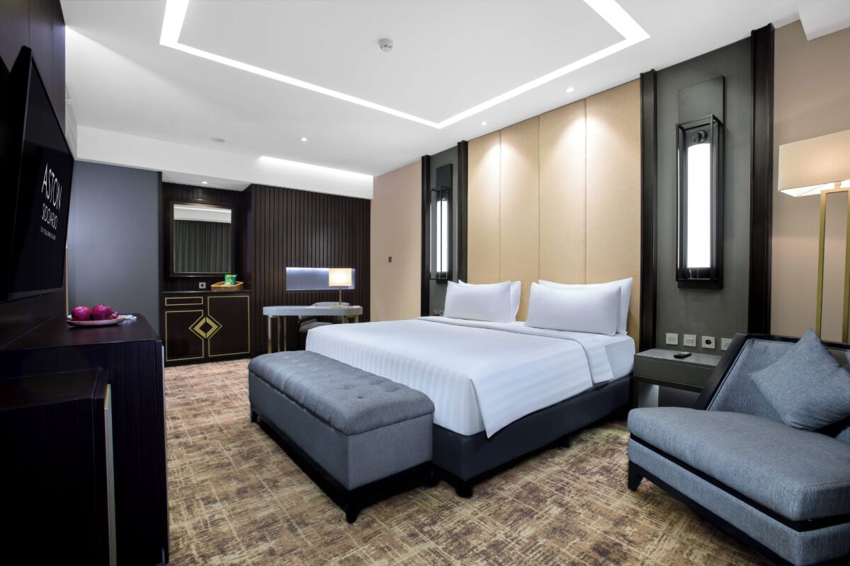 A modern hotel room with a large bed, a desk, a TV, and a seating area.
