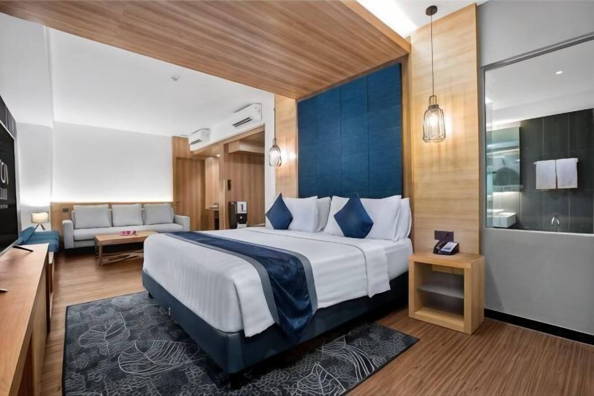 A modern hotel room with a large bed, a desk, a sofa, and a bathroom.