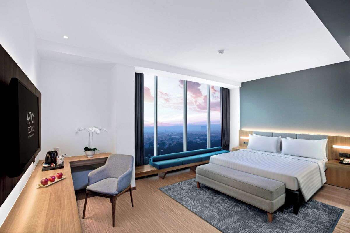 Una habitación de hotel moderna con una cama grande, una zona de estar, un escritorio y un televisor.