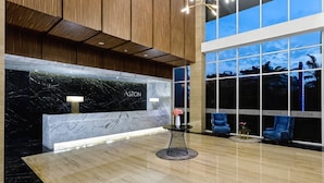 A modern lobby with a marble reception desk, wooden paneling, and large windows offering views of the cityscape. - Aston Sidoarjo City Hotel & Convention Center (Sidoarjo)