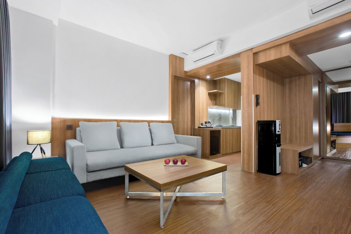 A modern living room with a sofa, a coffee table, and a kitchen area with a refrigerator.