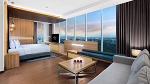 A modern hotel room with a large bed, a sofa, a coffee table, and a TV. The room has large windows with a city view. - Aston Sidoarjo City Hotel & Convention Center (Sidoarjo)