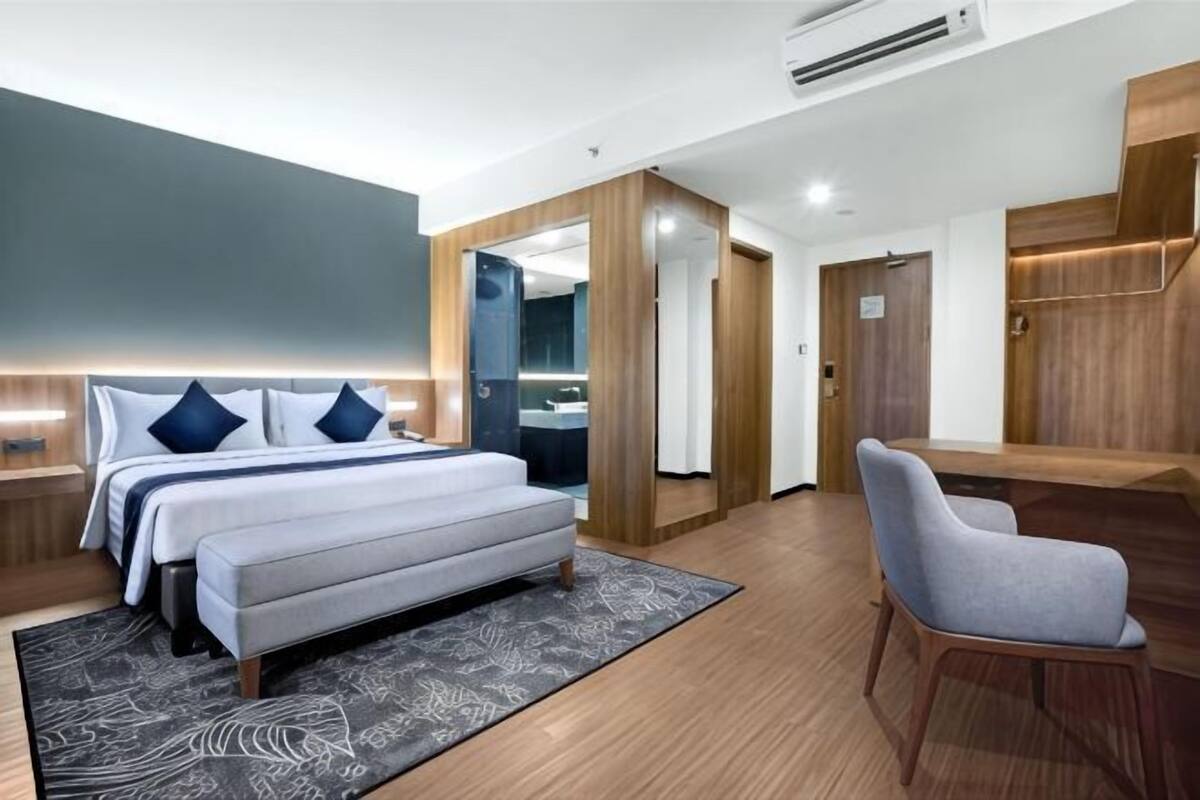 A hotel room with a bed, a desk, a chair, and a bathroom visible through an open door.