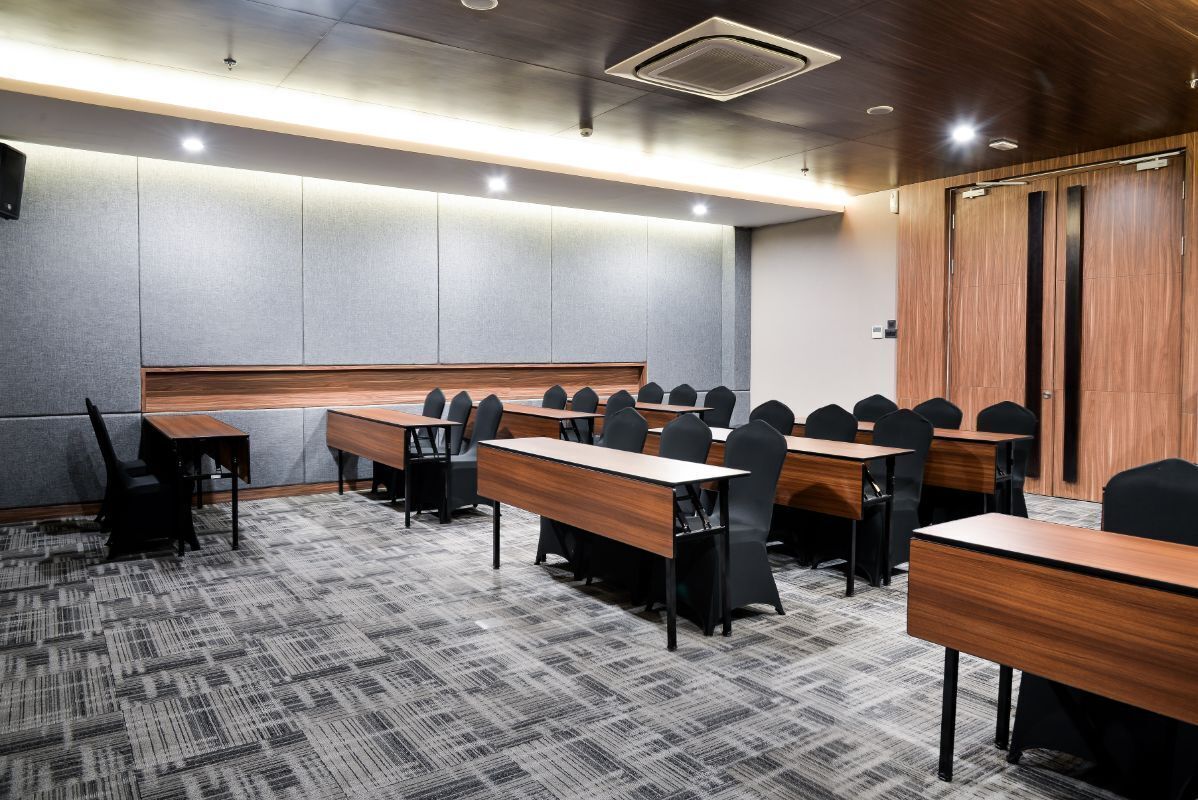 A conference room with multiple tables and chairs, a wooden panel wall, and a carpeted floor.