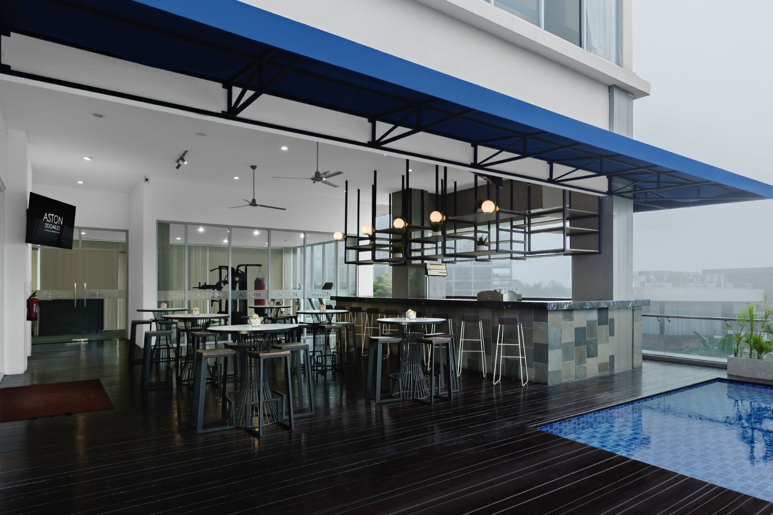 A modern indoor pool area with a bar and seating, large windows, and a high ceiling.