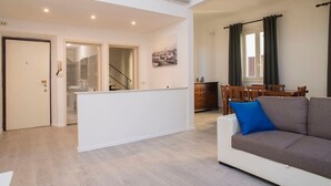 Una sala de estar moderna con un sofá, un comedor con mesa y sillas, una cocina con mostrador y fregadero, y una escalera que sube a un piso superior.