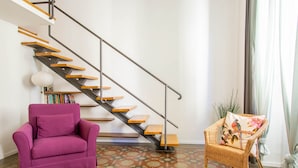 Un interior moderno con una escalera, un sillón púrpura, una silla de mimbre y un suelo estampado.