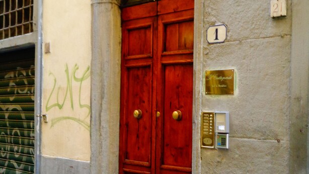 Una puerta roja con un aldabón de bronce, una placa y un cartel con un número.
