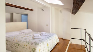 Un dormitorio con cama, tragaluz, viga de techo de madera, escalera y baño con pared de azulejos azules.