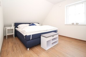 A bedroom with a bed, a bedside table, a nightstand, a window, and a wooden floor. - Holiday apartment "time for two" in Greetsiel (Greetsiel)
