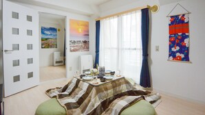 A room with a dining table set with plates, glasses, and a bottle. There is a window with curtains, a door with a view of another room, and a wall with a poster. - KIYAZA City Sapporo (Sapporo)