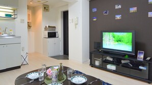 A modern living room with a dining area, a kitchen in the background, and a television on a black stand. - KIYAZA City Sapporo (Sapporo)