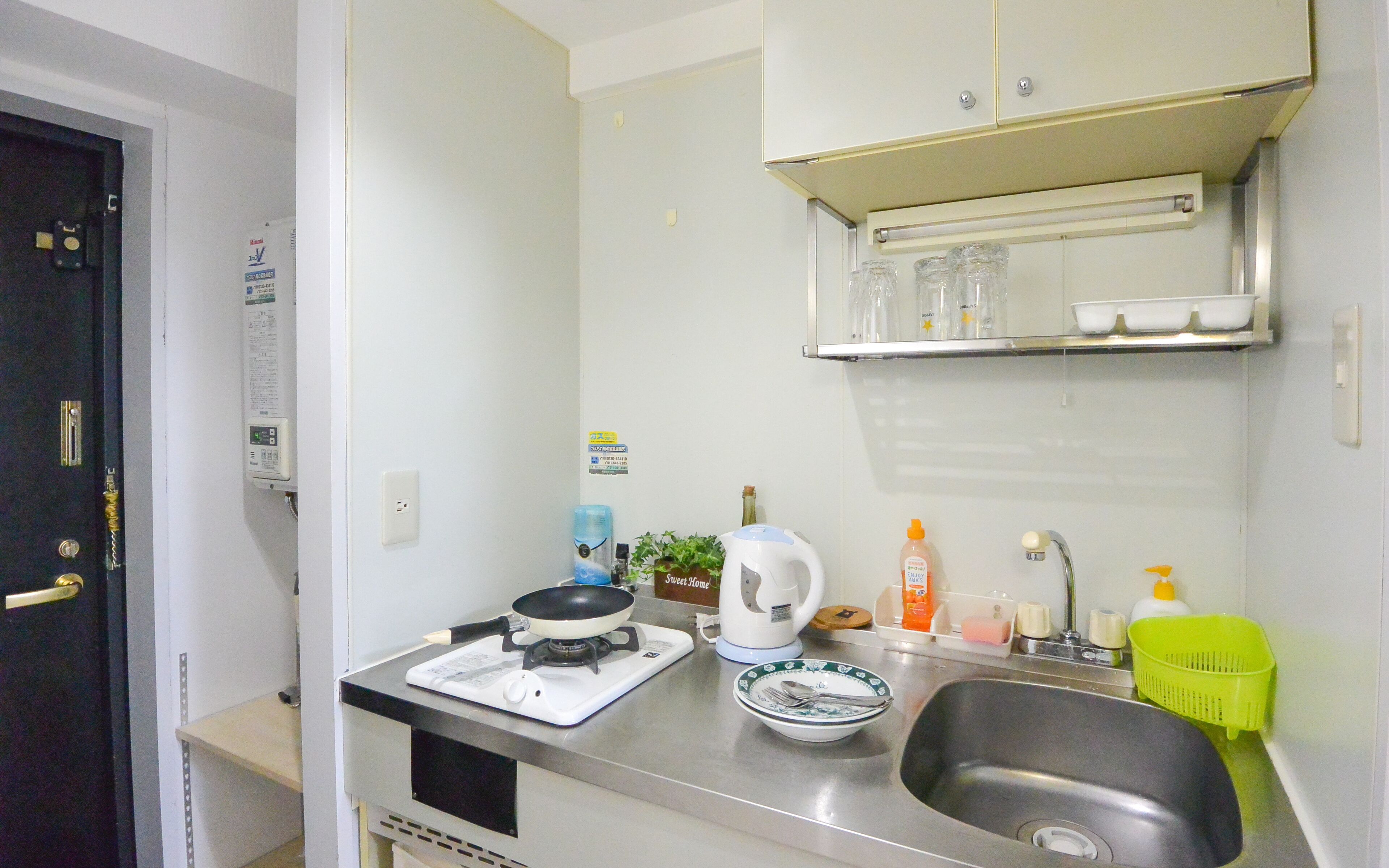 A compact kitchenette with a gas stove, a kettle, a sink, and a small countertop.