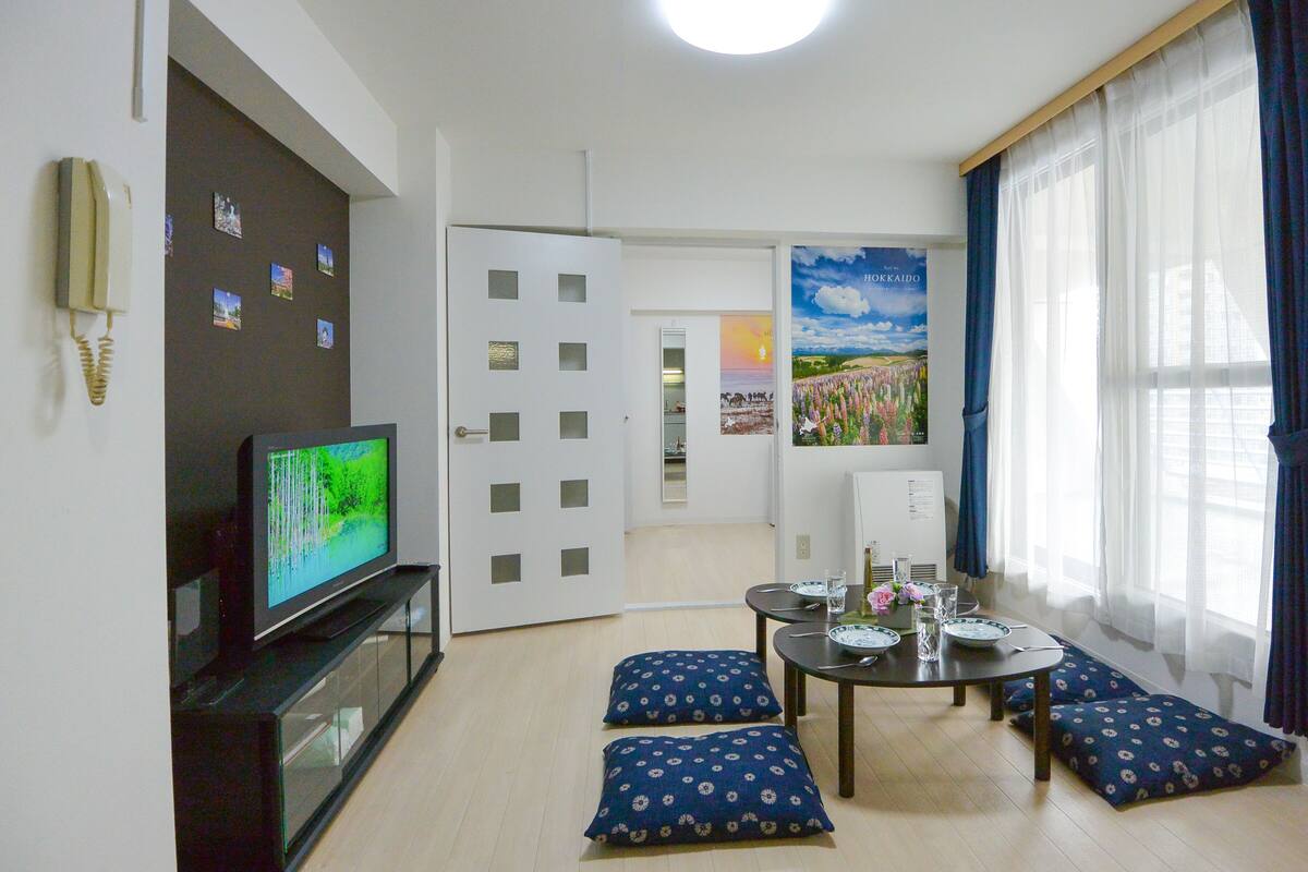 Olohuone, jossa on televisio, ruokapöytä tuoleineen ja taustalla keittiö.