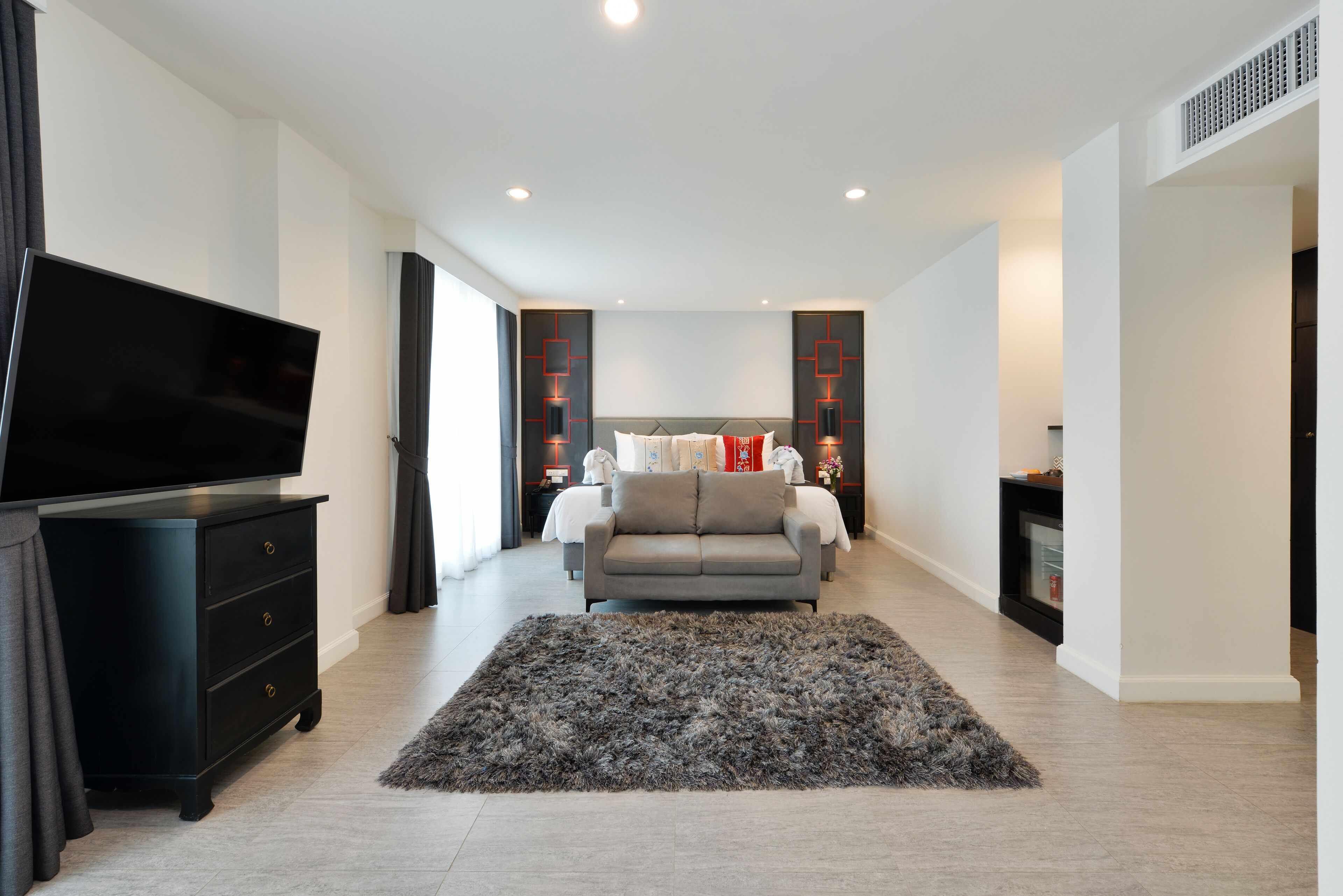 A modern hotel room with a flat-screen TV, a sofa bed, a large rug, and a TV stand.