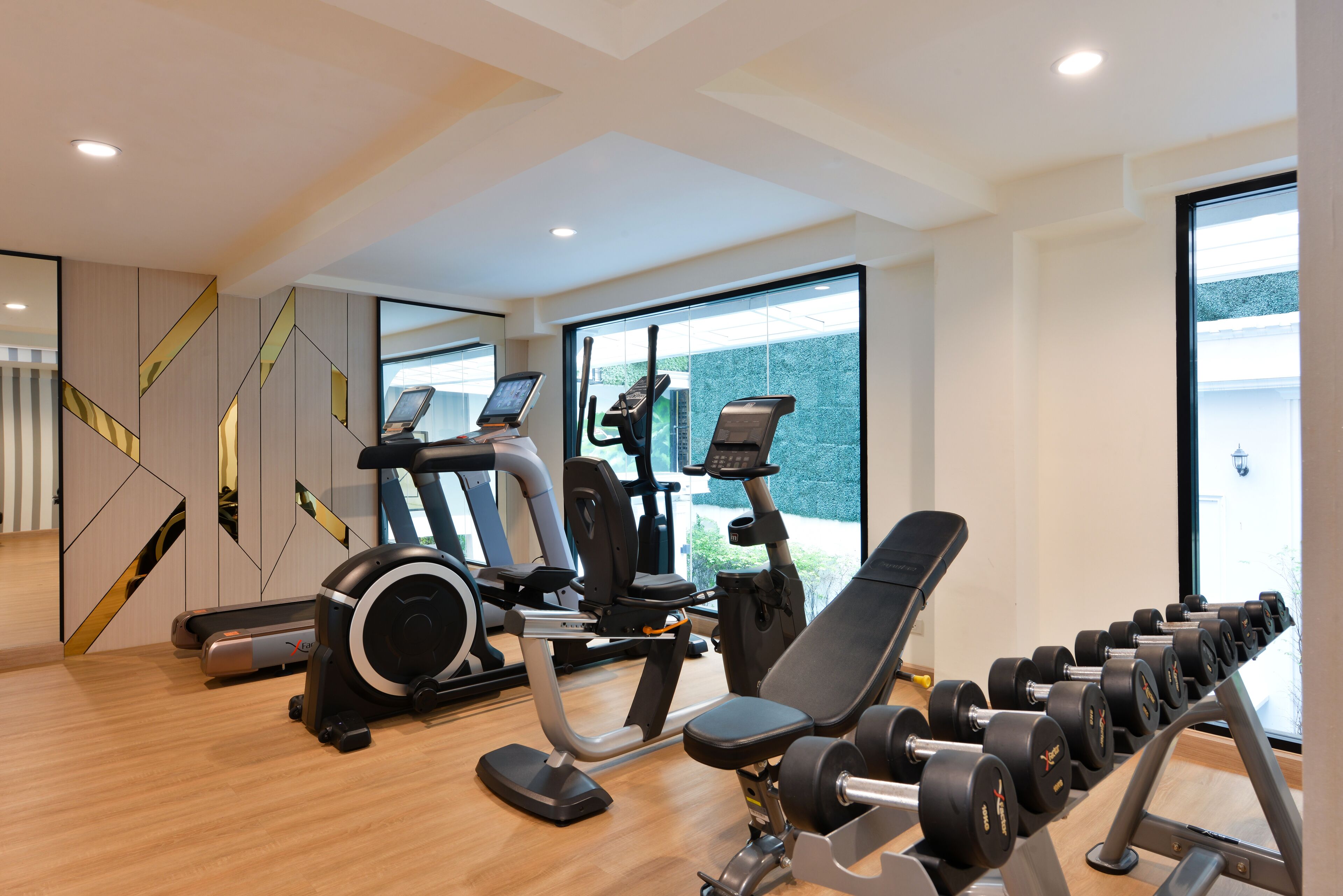 Un gimnasio moderno con máquinas de cardio, equipo de levantamiento de pesas y amplias ventanas que ofrecen luz natural.